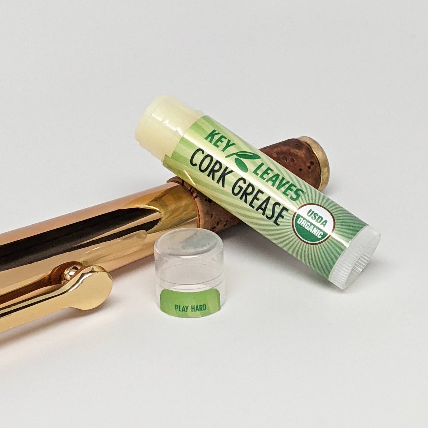 Organic all-natural cork grease from Key Leaves. The tube of cork grease is open and laying on the neck of a rose brass alto sax.