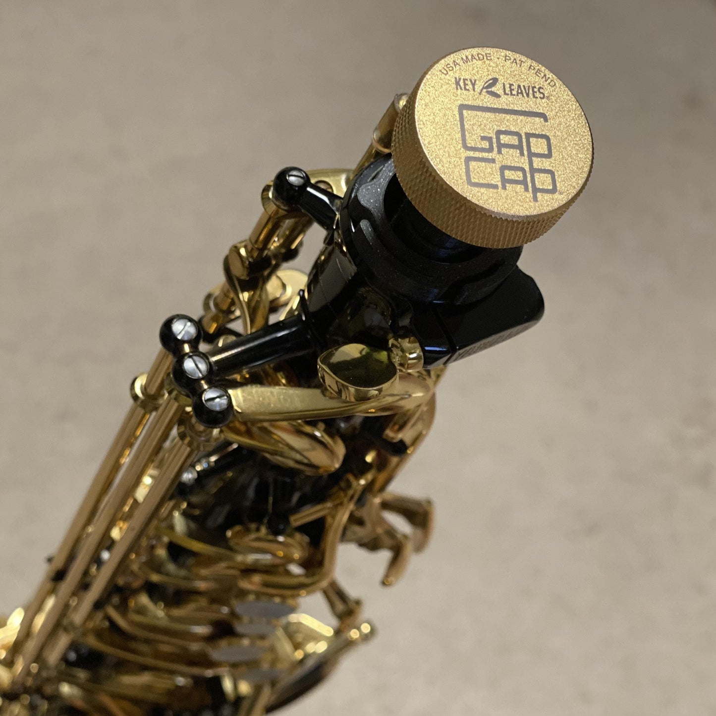A gold plated GapCap® saxophone end plug shown on a black lacquer alto saxophone.